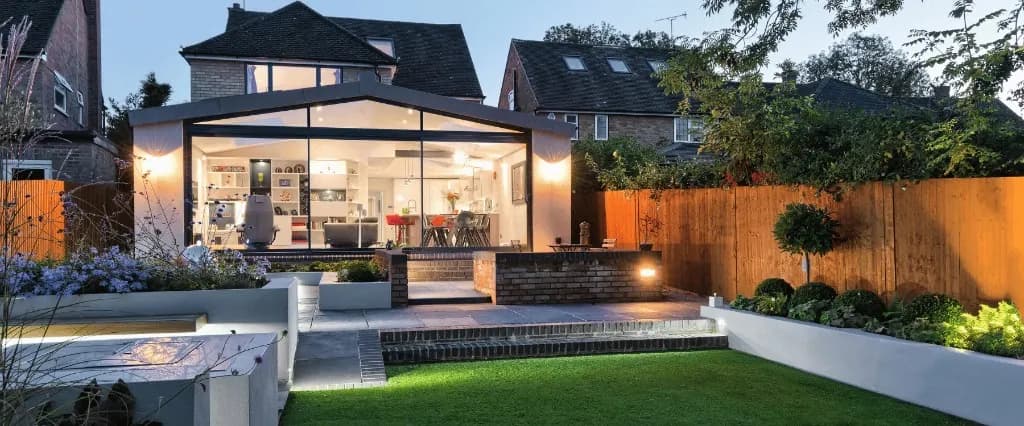 Rear home addition with glass facade, stone patio, and landscaped garden at dusk in Rosedale, Toronto